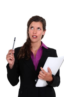 Young businesswoman looking upwards with notepad and pen clipart