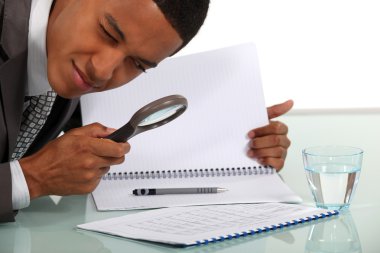 Man examining a document with a magnifying glass clipart