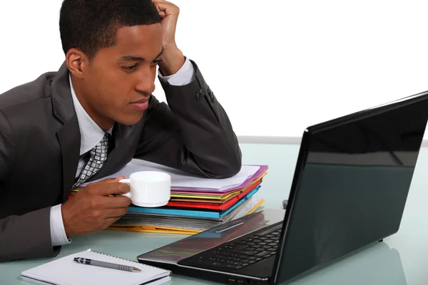 Az afrikai-amerikai üzletember, iszik egy kávét, miközben keresi a laptop. — Stock Fotó