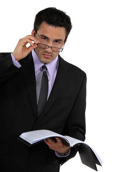 Empresário olhando sobre seus óculos e segurando sua agenda — Fotografia de Stock