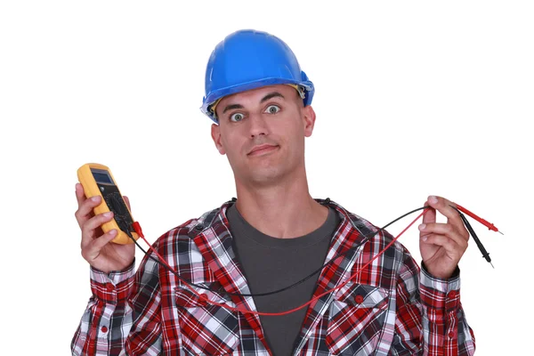 A wide-eyed tradesman holding a multimeter — Stock Photo, Image