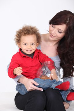 A cute kit eating cookie on his mother's lap. clipart