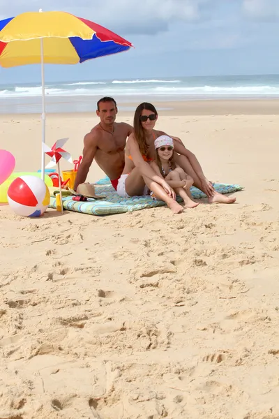 Família sentou-se na praia por guarda-sol — Fotografia de Stock