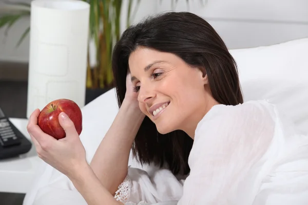 Жінка тримає яблуко, сидячи на дивані — стокове фото