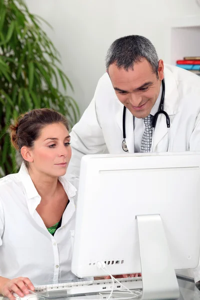 Doutor e uma secretária médica assistindo um computador — Fotografia de Stock