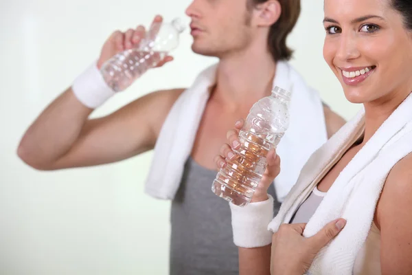 Pareja bebiendo botellas de agua en el gimnasio — Foto de Stock