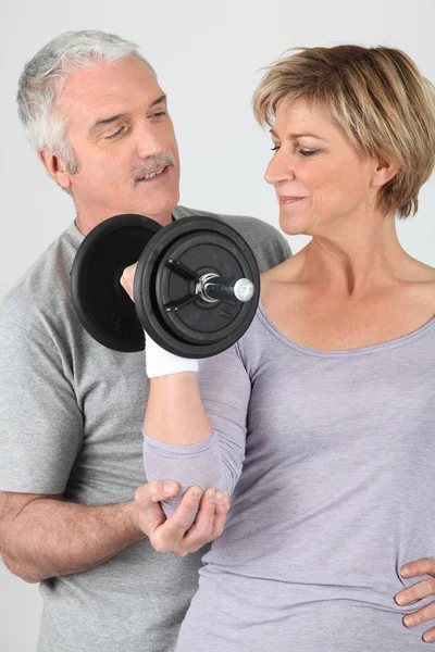 Man helping a woman lift a dumbbell — Stock Photo, Image