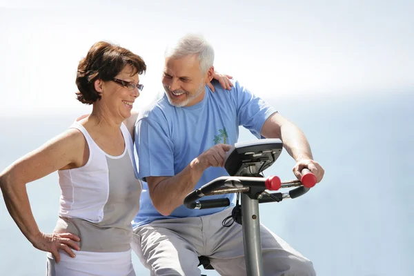 Casal de idosos com uma bicicleta de exercício — Fotografia de Stock