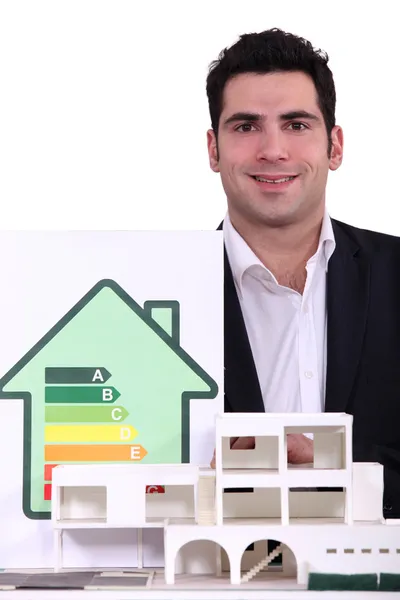 Arkitekt poserar nära modell visar hus med energi betyg — Stockfoto