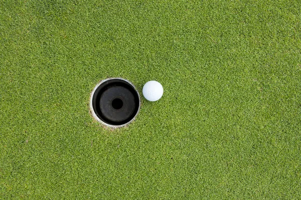 Golfball på kanten av hullet. – stockfoto