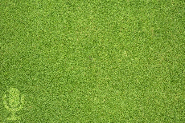Значок микрофона на зеленой текстуре травы и фоне — стоковое фото