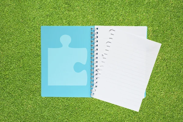 Livro com jigsaw ícone no fundo da grama — Fotografia de Stock