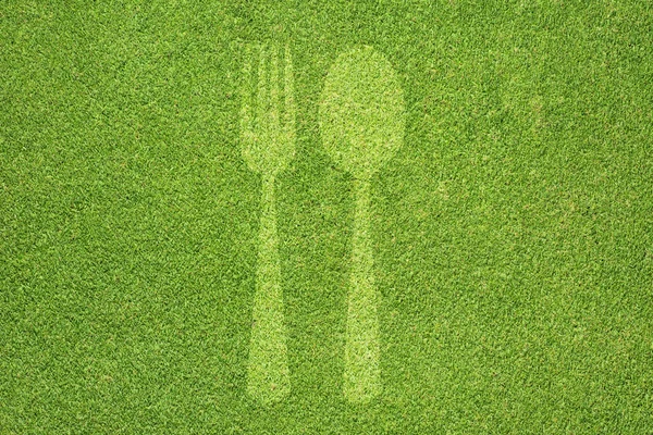 Значок вилки и ложки на зеленой текстуре травы и фоне — стоковое фото