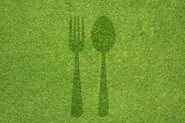 Піктограма вилки та ложки на зеленій текстурі трави та фоні — стокове фото