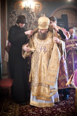 Two monks help the Bishop to robe