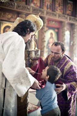 Orthodox bishop gives communion to a little boy clipart