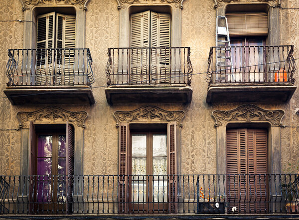 A few old-fashioned balconies with steel fence and with different things on, placed above each other on the pastel wall with ornamental pattern