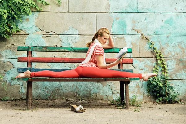 Спортивная женщина читает книгу и делает упражнения на растяжку — стоковое фото