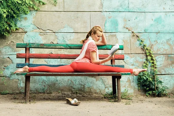 Donna sportiva sta leggendo un libro e facendo esercizio di stretching su Immagini Stock Royalty Free