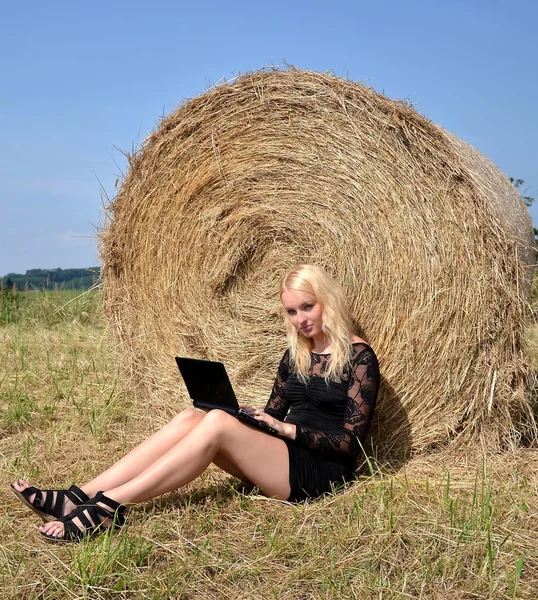 Sexy Frau mit einem Laptop bei einem Heustapel an einem Sommertag — Stockfoto