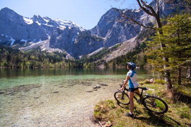 Yaung woman riding a bike beside Alpine lake clipart