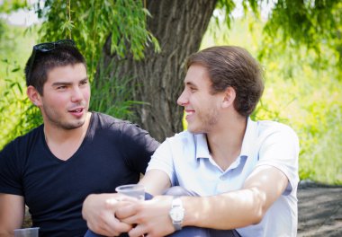 Two guys relaxing alongside a nature drink coffee clipart