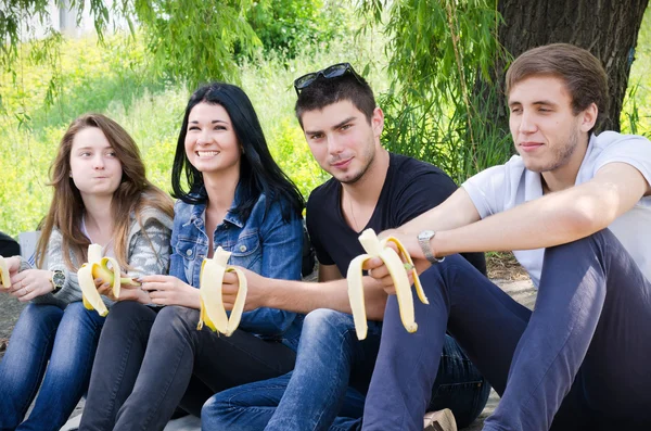 Row of friends sitting together eat banana — Stock Photo, Image