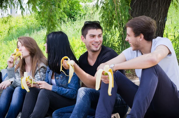 Fila di amici seduti insieme mangiare banana — Foto Stock
