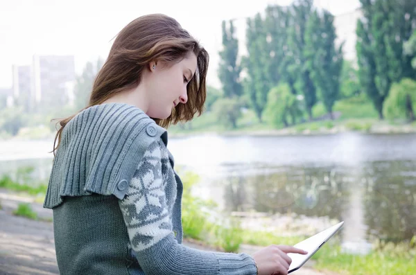 Девушка сидит на улице, используя планшет с сенсорным экраном вдоль реки — стоковое фото
