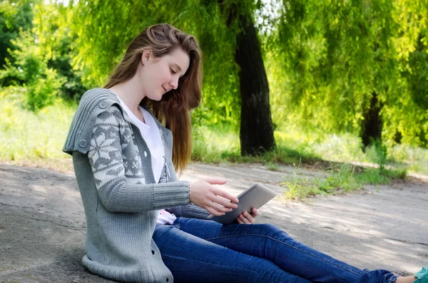 Flicka sitter utomhus med hjälp av en pekskärm tablet — Stockfoto