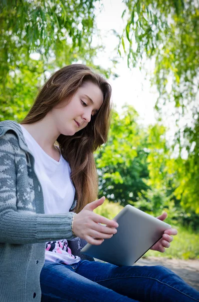 Tjej som arbetar på en tablett i grön park sommaren — Stockfoto