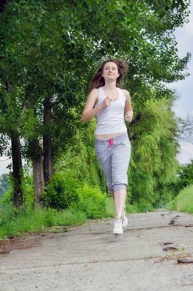 Jovem mulher correndo através de um parque — Fotografia de Stock