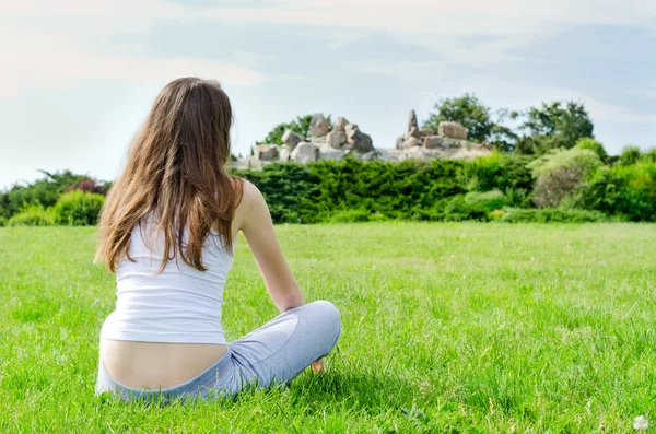 Женщина сидит на зеленой лужайке в парке — стоковое фото