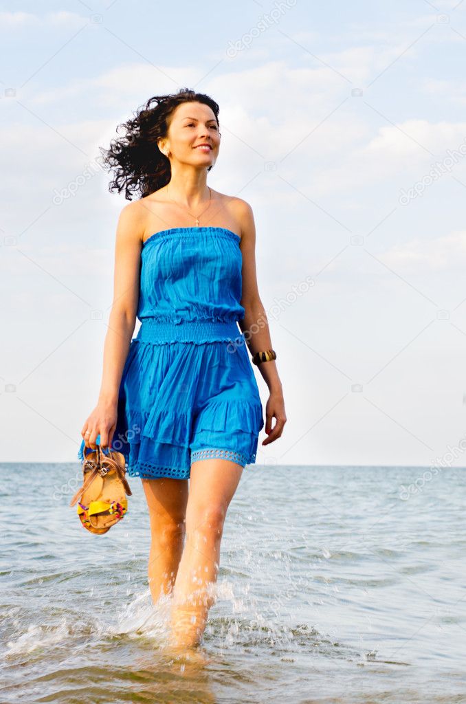 Woman running along the edge of the surf in hand beach slippers
