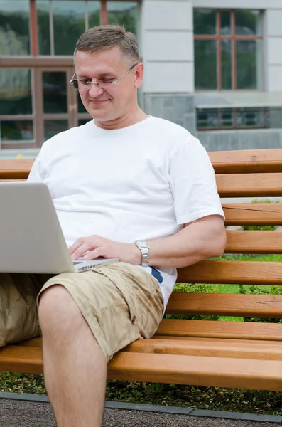 Άνδρας κάθεται στο ξύλινο πάγκο χρησιμοποιώντας ένα φορητό υπολογιστή — Φωτογραφία Αρχείου