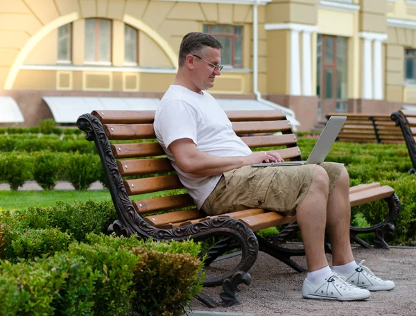 Człowiek za pomocą laptopa na ławce w publicznych — Zdjęcie stockowe