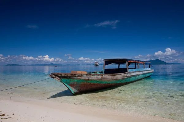 Een eenzame houten boot afgemeerd op het kristal heldere water van een tropisch eiland. — Stockfoto