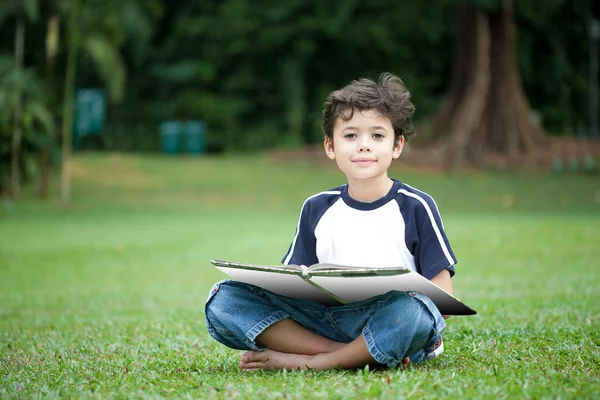 Νεαρό αγόρι απολαμβάνει το βιβλίο του στο υπαίθριο πάρκο — Φωτογραφία Αρχείου
