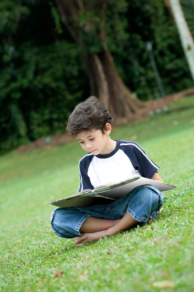 Νεαρό αγόρι απολαμβάνει το βιβλίο του στο υπαίθριο πάρκο — Φωτογραφία Αρχείου