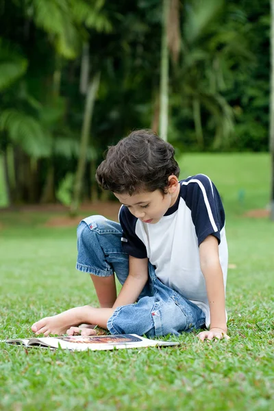 Ung pojke njuter av sin läsning bok i utomhus park — Stockfoto