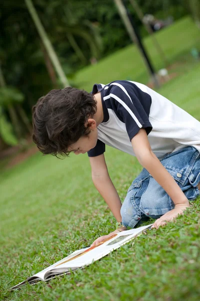 Młody chłopiec korzystających jego książka do czytania w parku na świeżym powietrzu — Zdjęcie stockowe