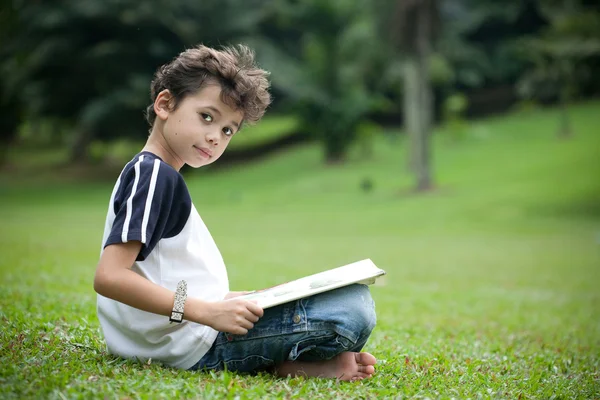 Genç çocuk açık hava parkında kitap okumaktan zevk alıyor. — Stok fotoğraf
