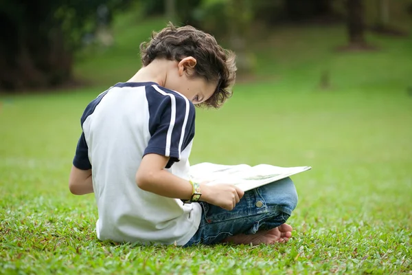 Niño disfrutando de su libro de lectura en el parque al aire libre — Foto de Stock