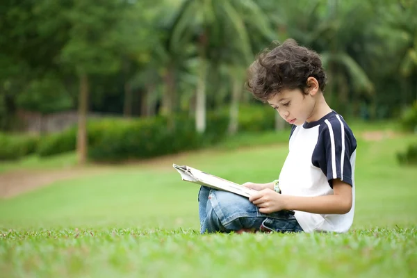 Genç çocuk açık hava parkında kitap okumaktan zevk alıyor. — Stok fotoğraf