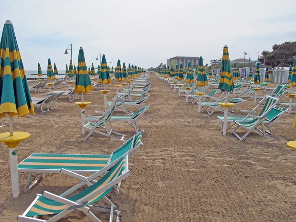 Closed Sun umbrellas and deck chairs and beds from the sea on a — Stock Photo, Image