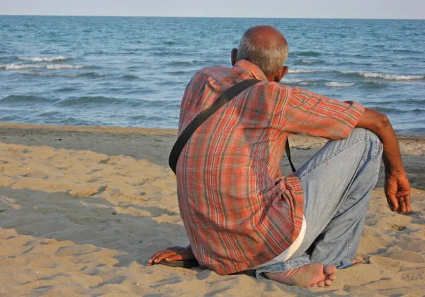 Un homme assis sur le sable attend — Photo