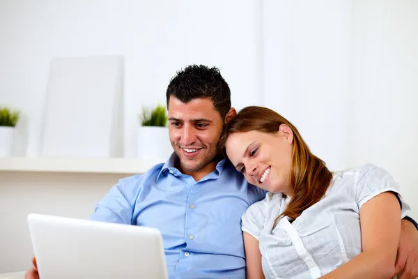 Lyckliga unga paret sitter på soffan med en bärbar dator — Stockfoto