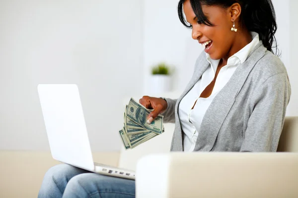Удивлённая женщина с долларами, ищущая ноутбук — стоковое фото