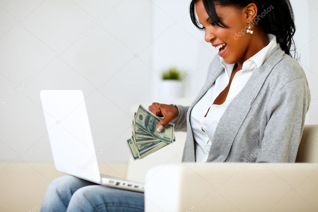 Surprised woman with dollars looking to laptop
