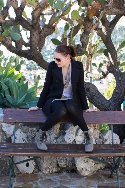Jonge vrouw zittend op een bankje in een botanische tuin — Stockfoto